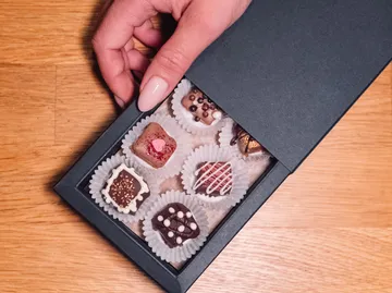 Hand öffnet Pralinenschachtel mit verschiedenen Pralinen.