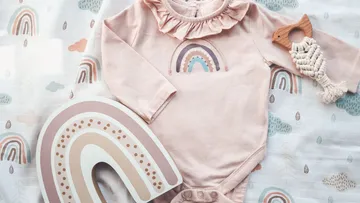Rosa Baby-Outfit mit Regenbogen und Holzspielzeug.