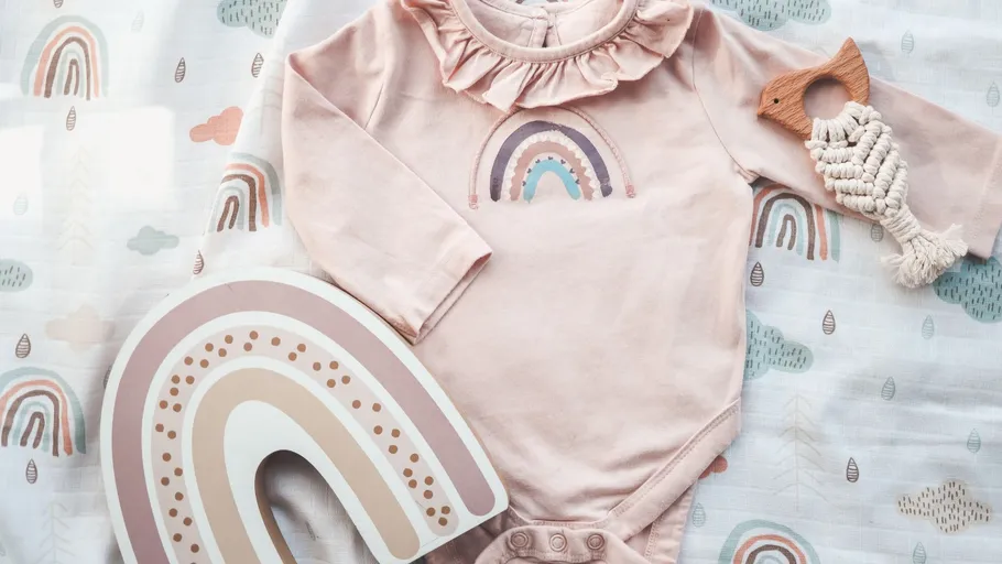 Rosa Baby-Outfit mit Regenbogen und Holzspielzeug.