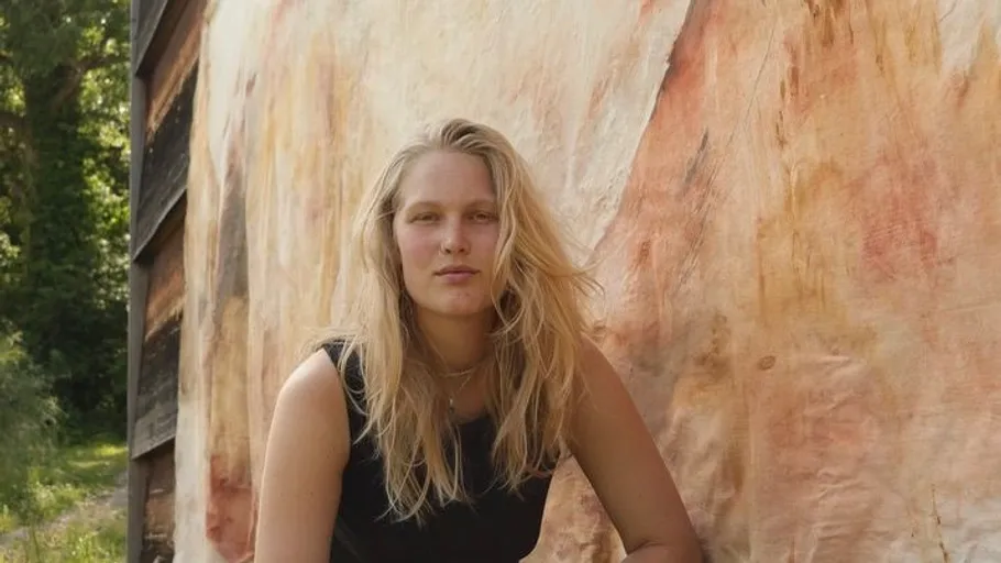 Person sitting near a textured wall outdoors.