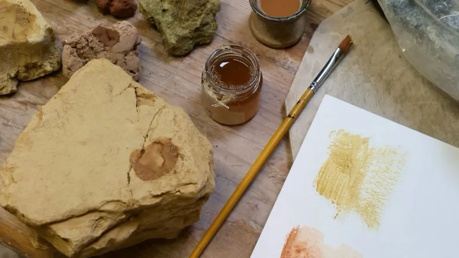 Steine, Pigmentgläser und bemaltes Papier auf Tisch.