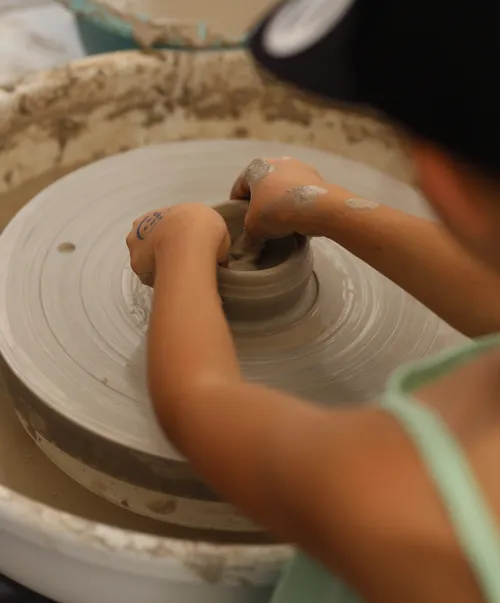 Child shaping clay on a pottery wheel.