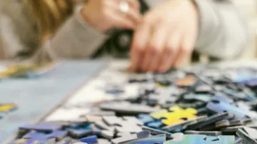 Hand assembling jigsaw puzzle on table.
