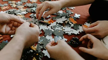 Hände setzen ein Puzzle auf rotem Untergrund zusammen.