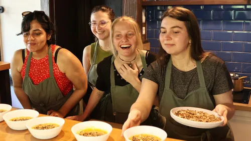 Four women serving dishes at a wooden countertop.