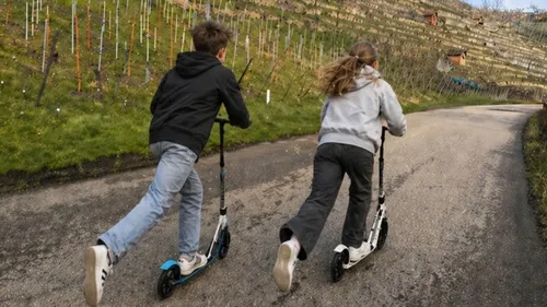 Two kids riding scooters uphill on a path.