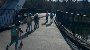 Children riding scooters on a bridge outside.