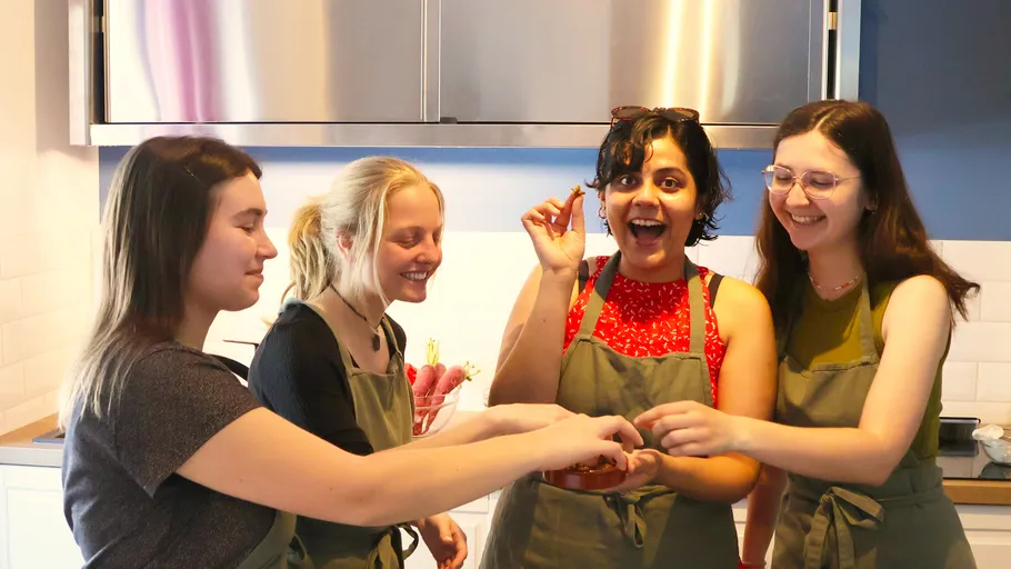 Vier Frauen in Schürzen lachen in einer Küche.