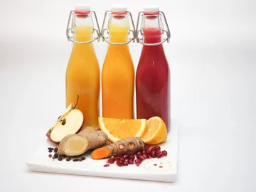There are three bottles of drinks with fresh fruit next to it.