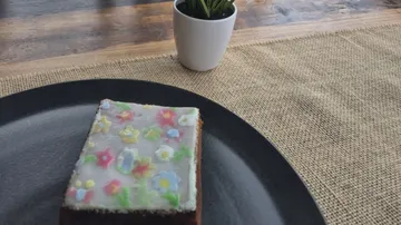 Mit Blumen dekoriertes Kuchenstück auf schwarzem Teller.