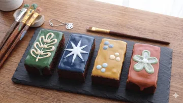 Vier dekorierte Kuchen auf einer Schieferplatte.