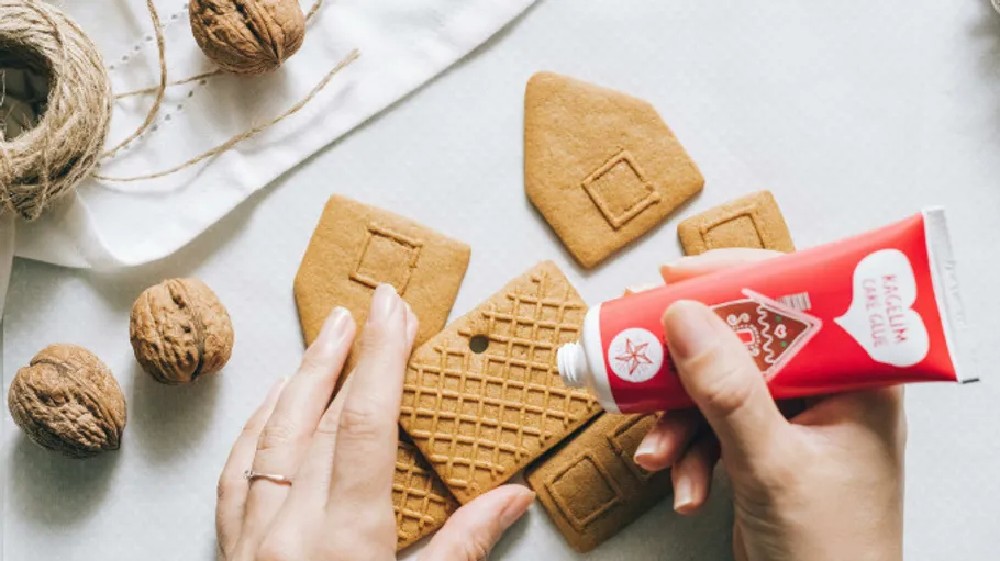 Hands assembling gingerbread house with icing tube.