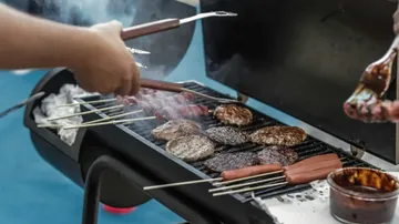 Hände grillen Burger und Würstchen im Freien.