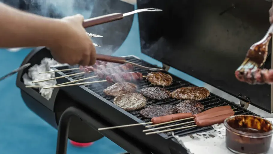 Hands grilling burgers and hot dogs outdoors.