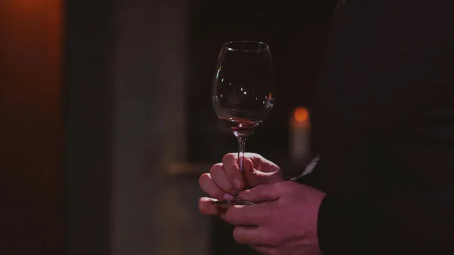 Person holding wine glass in dimly lit room.