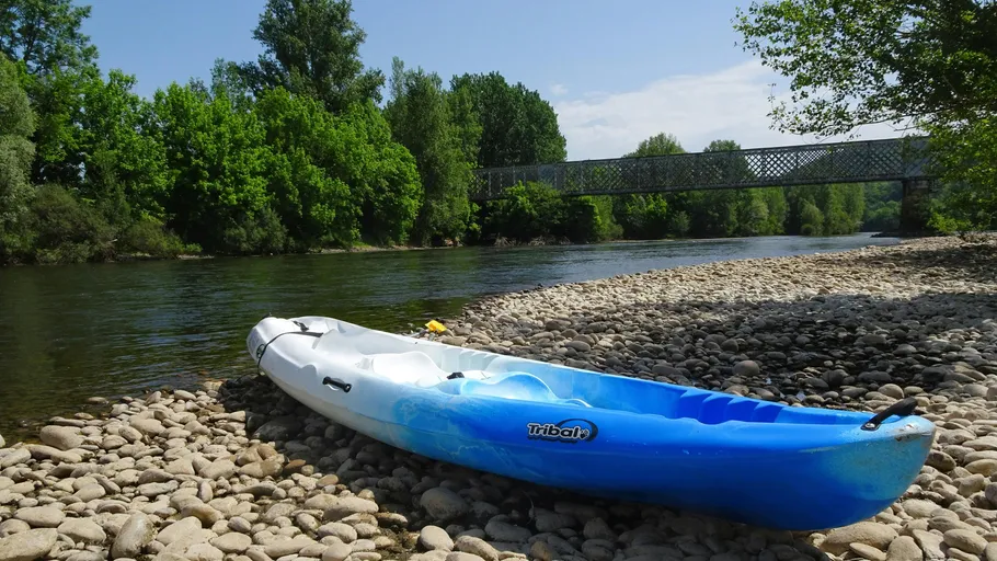 Kajak ruht auf Kieselsteinufer nahe Brücke.