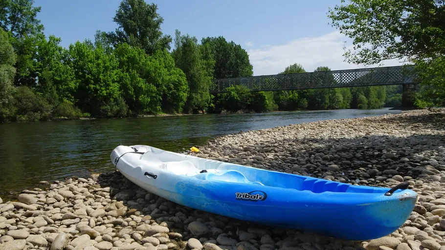 Blaues Kajak ruht auf steinigem Flussufer, unter Brücke.