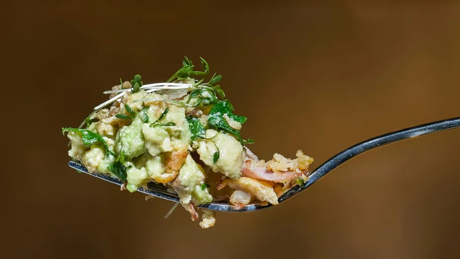 Fork holding avocado salad against brown background.