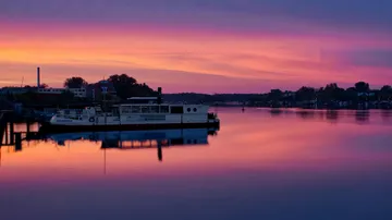 Boat docked on calm water at vibrant sunset.
