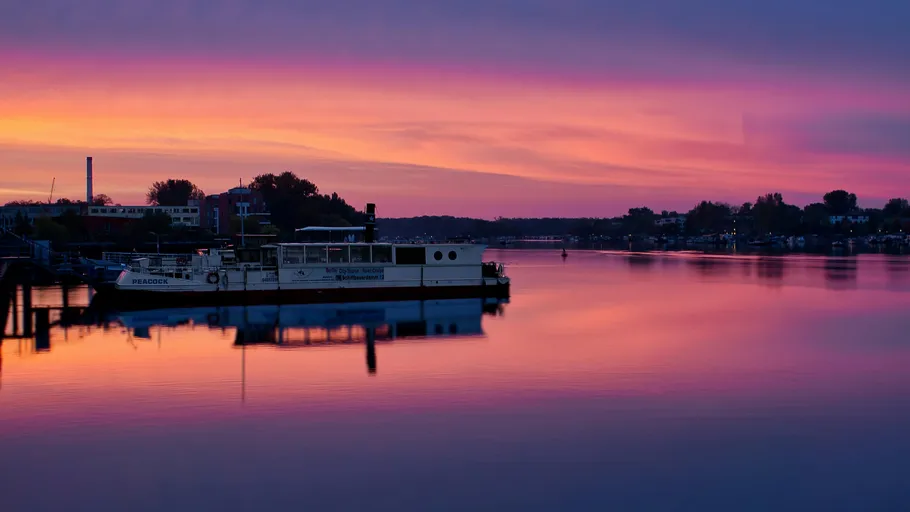 Boat docked on calm water at vibrant sunset.