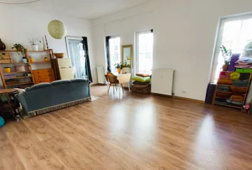 Geräumiges Zimmer mit Holzboden, Sofa und Regalen.