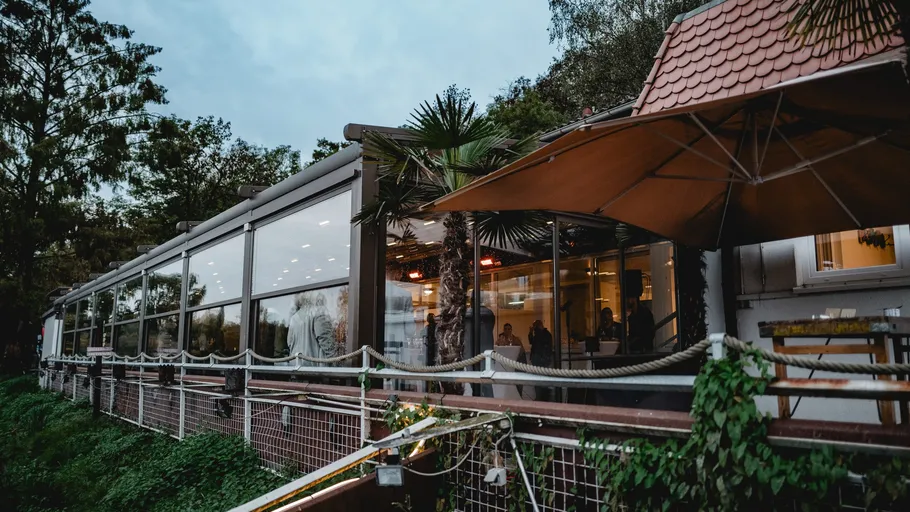 Modern outdoor cafe with glass walls, evening setting.