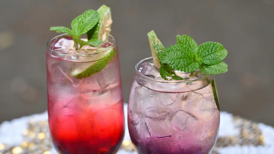 Zwei bunte Cocktails mit Minzdeko im Freien.