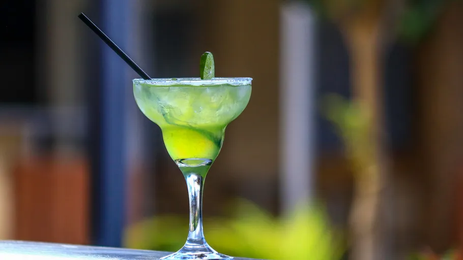 Green cocktail with lime on outdoor table.