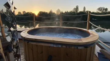 Wooden hot tub steaming on a lakeside deck.