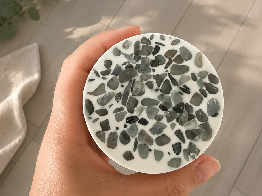 Hand holding terrazzo-patterned round object indoors.