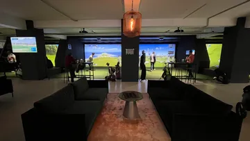 Personen spielen Golfsimulatoren in modernem Lounge-Bereich.