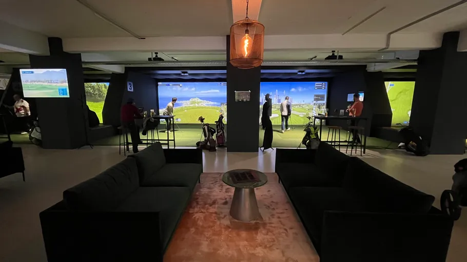 Personen spielen Golfsimulatoren in modernem Lounge-Bereich.