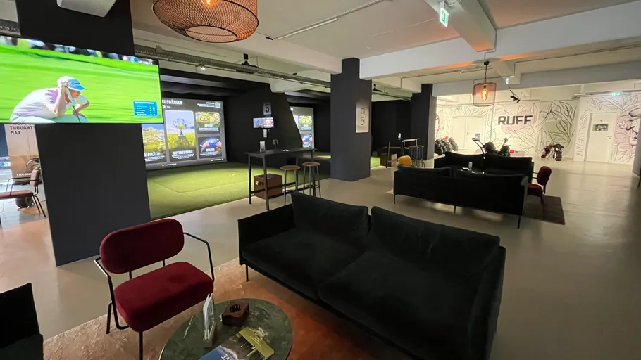 Moderner Indoor-Golf-Lounge mit Sitzgelegenheiten und Bildschirmen.
