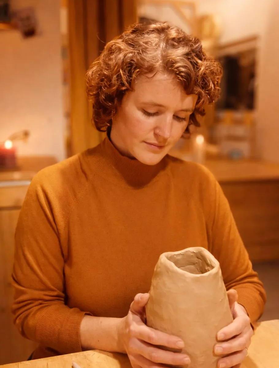 Woman shaping clay object at wooden table.