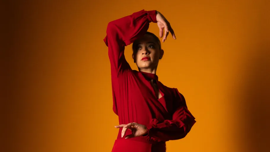 Person posing dramatically in red dress, orange background.