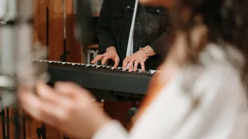 Person playing keyboard, blurred foreground hand.