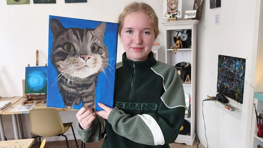 Person holds a cat painting in art studio.