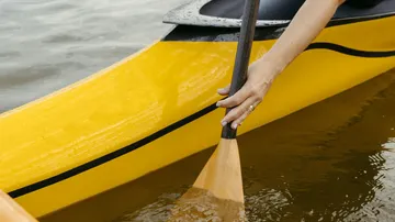 Hand paddelt gelbes Kajak auf Wasser.