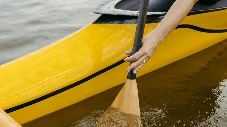 Hand paddelt gelbes Kajak auf Wasser.