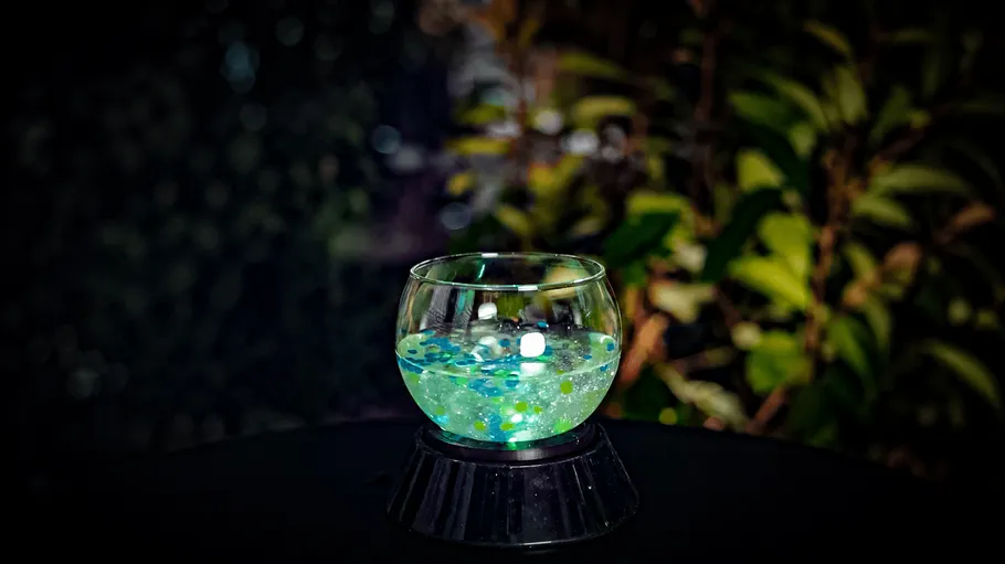 Glowing glass with colorful lights against foliage.