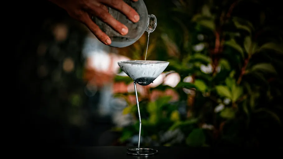 Hand pouring liquid into a martini glass.