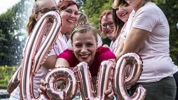 Smiling women holding 'love' balloon outdoors.