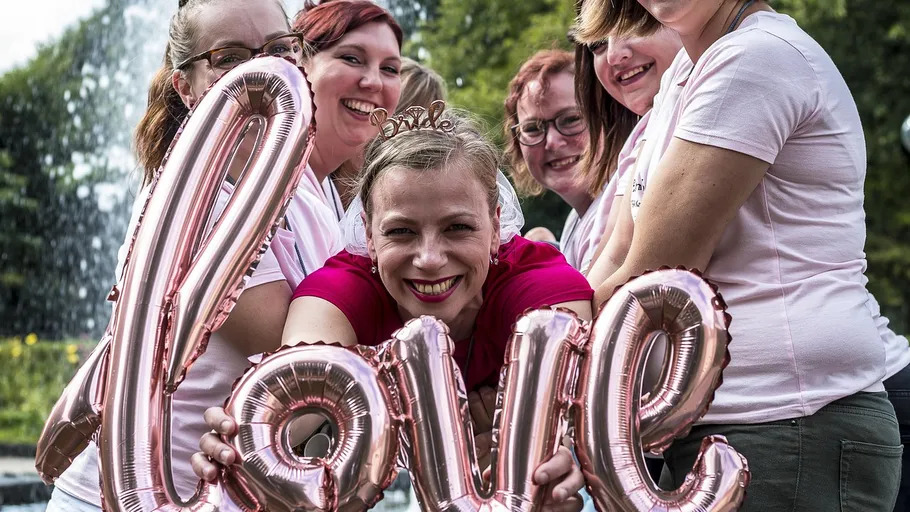 Smiling women holding 'love' balloon outdoors.