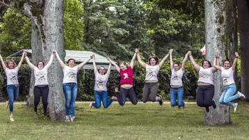 Gruppe von Frauen springt im Park, hält Hände.
