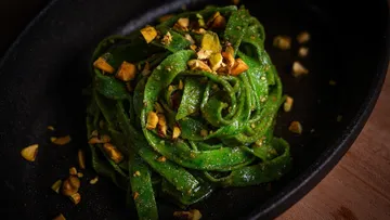 Green pasta topped with chopped nuts in black dish.