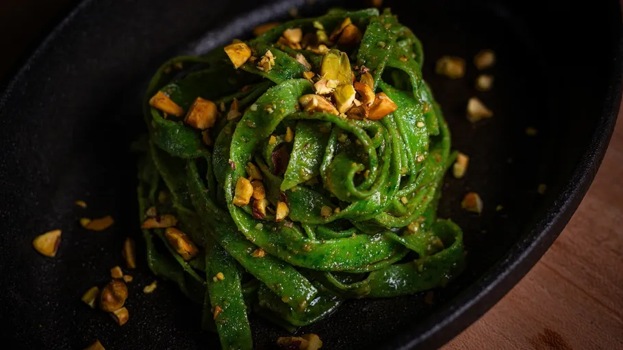Green pasta topped with chopped nuts in black dish.