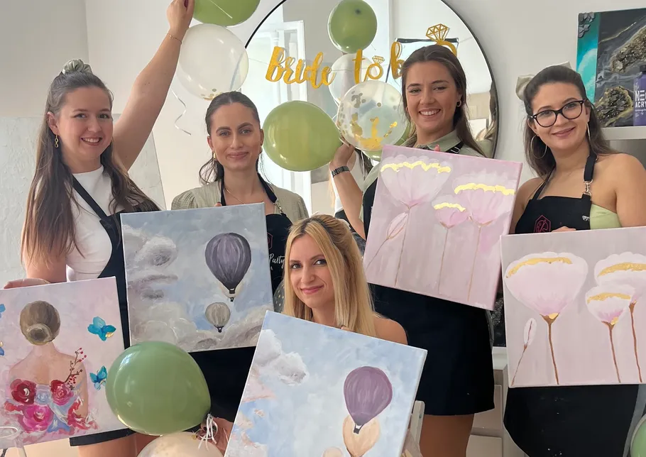 Fünf Frauen zeigen Gemälde auf einer Feier.