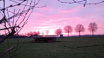 Anhänger auf Feld mit pinkem Sonnenuntergangshimmel.