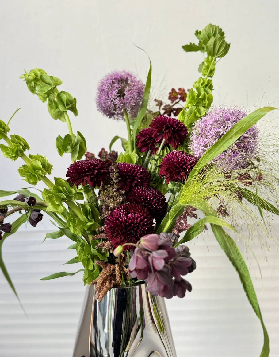 Blumenarrangement in einer glänzenden Vase, weißer Hintergrund.