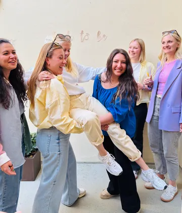 Group of women laughing, lifting another indoors.